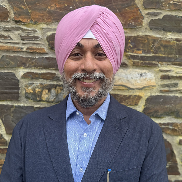 Gulzar Singh pictured in a dark blue suit jacket and sky blue shirt. He is pictured against a stone brown wall.