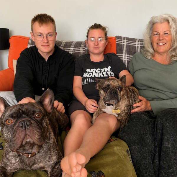 Shared Lives Carer Jan Shaw saw on the sofa with Jordan and Lucy who she supports along with french bull dogs Margot and Basil. Basil is in the foreground. All looking relaxed.